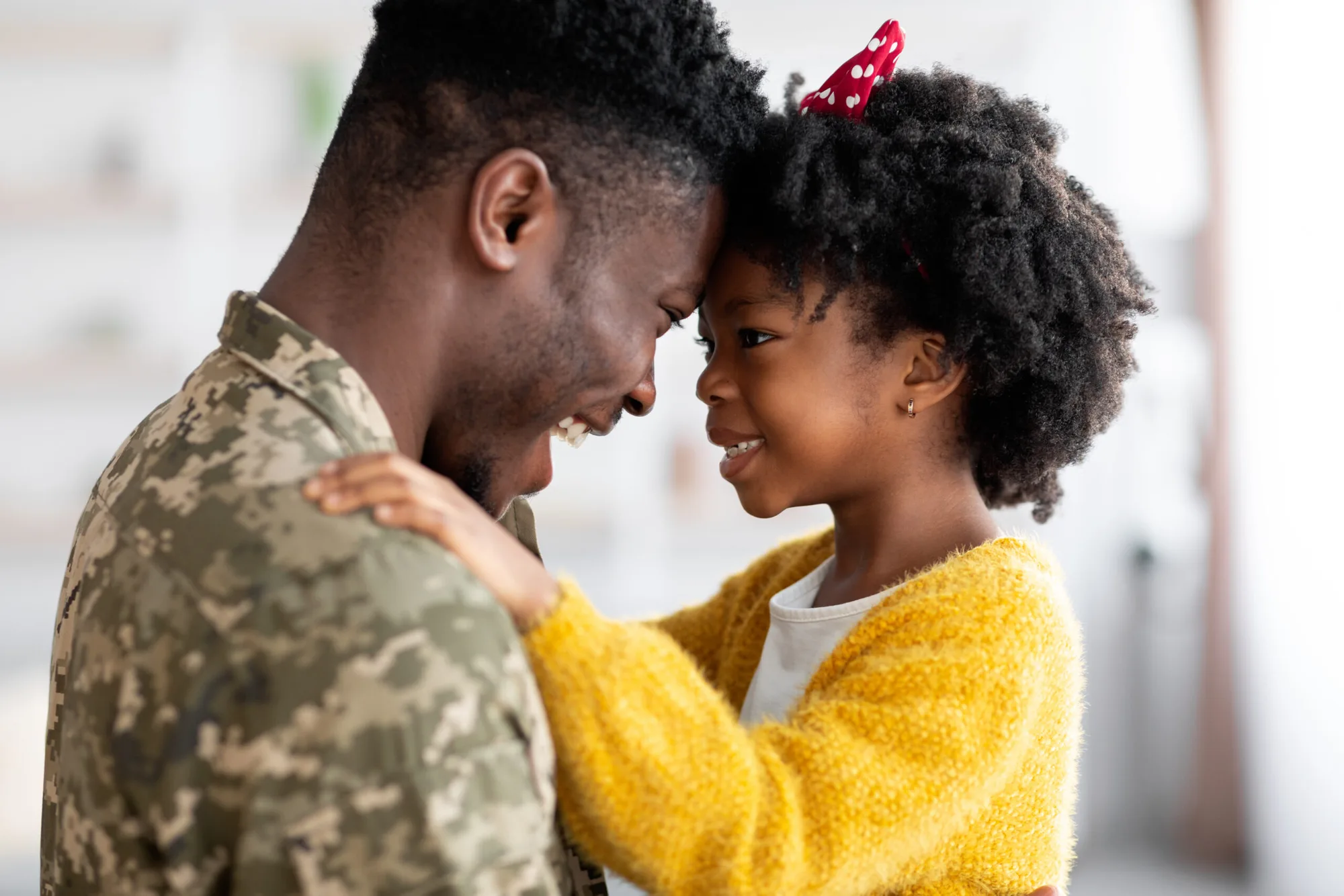 A soldier in uniform pressing his forehead to his smiling young daughter